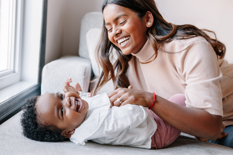 mother tickling toddler on couch